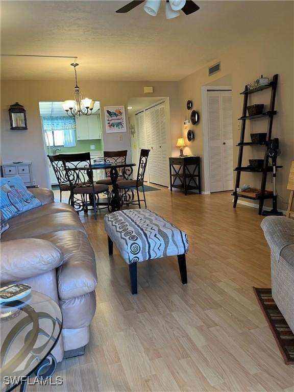 living room with visible vents, light wood finished floors, and ceiling fan with notable chandelier