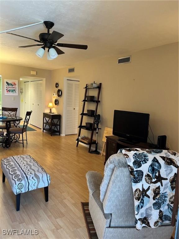 living room featuring light wood-style flooring, visible vents, and a ceiling fan