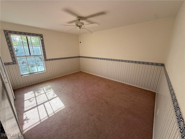 unfurnished room featuring a ceiling fan, wainscoting, and carpet flooring