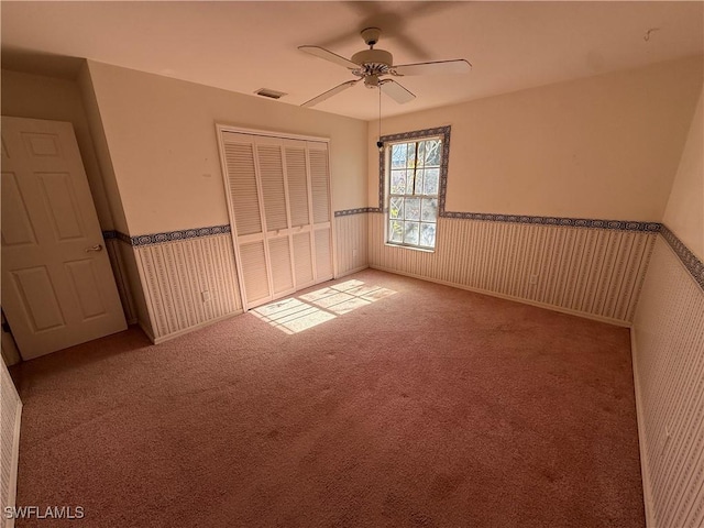 unfurnished bedroom featuring carpet, a closet, wainscoting, and visible vents