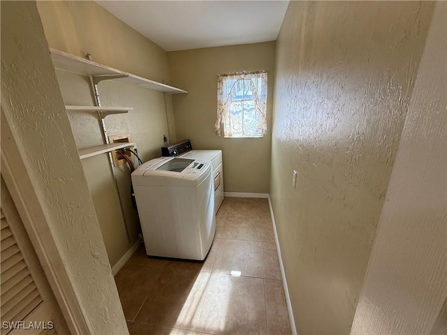 clothes washing area with laundry area, light tile patterned floors, baseboards, washer and clothes dryer, and a textured wall