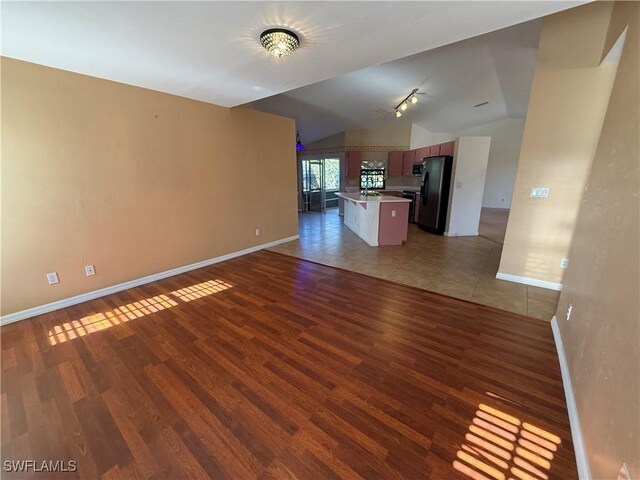 unfurnished living room featuring lofted ceiling, track lighting, wood finished floors, and baseboards