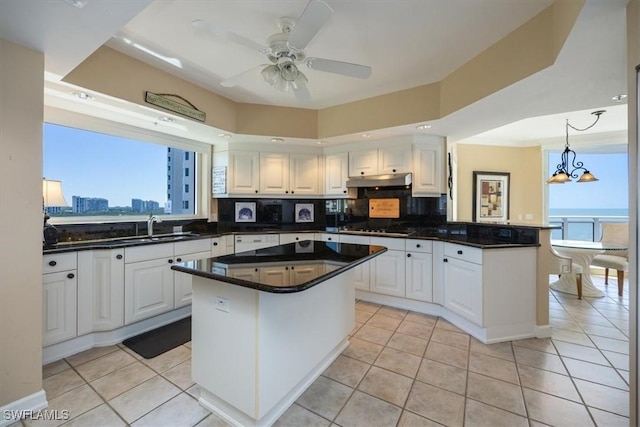 kitchen featuring a peninsula, gas stovetop, a sink, decorative backsplash, and under cabinet range hood