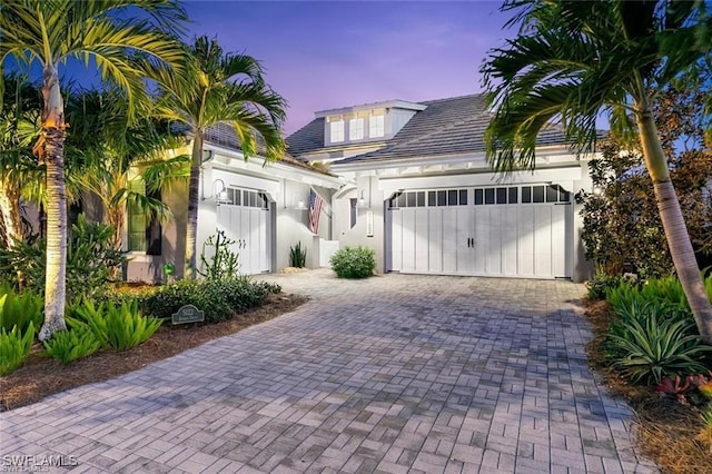 view of front facade featuring stucco siding, decorative driveway, and a garage