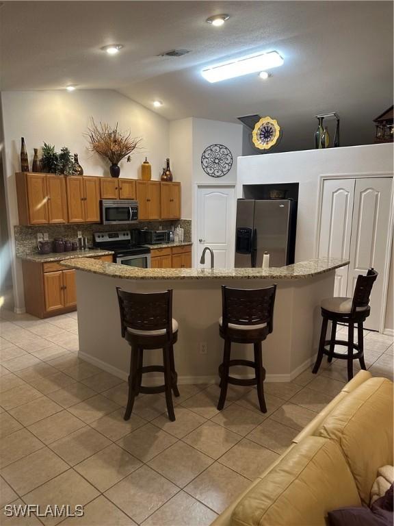 kitchen featuring light tile patterned floors, tasteful backsplash, a kitchen breakfast bar, vaulted ceiling, and stainless steel appliances