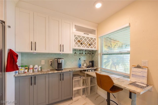 kitchen with white cabinets, tasteful backsplash, marble finish floor, and light stone counters