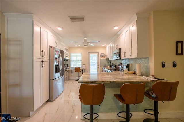 kitchen with visible vents, white cabinetry, stainless steel appliances, a peninsula, and light stone countertops