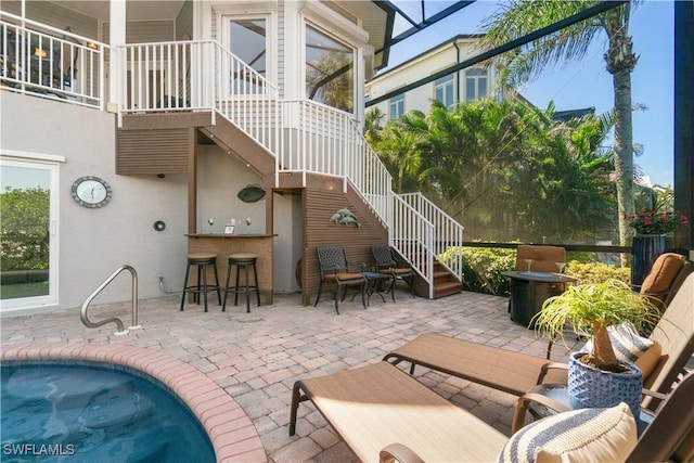 view of patio featuring a lanai, stairway, an outdoor pool, and outdoor dry bar