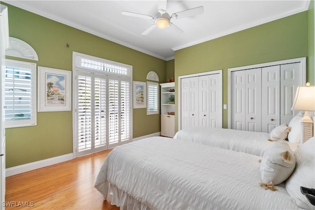 bedroom featuring crown molding, ceiling fan, baseboards, multiple closets, and wood finished floors