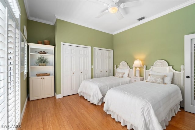 bedroom with a ceiling fan, visible vents, light wood finished floors, ornamental molding, and two closets