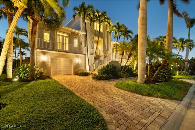 view of front of home featuring stairway, an attached garage, stucco siding, a front lawn, and decorative driveway