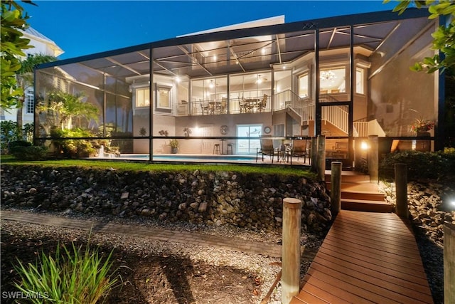 back of house at night with glass enclosure, a patio area, and an outdoor pool