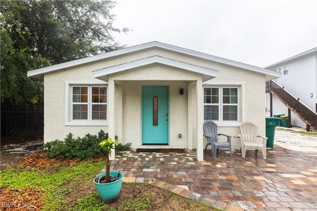 bungalow featuring a patio area, stairs, and stucco siding