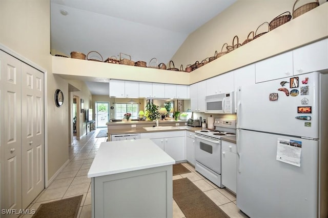 kitchen featuring light tile patterned flooring, a sink, white cabinets, white appliances, and a peninsula