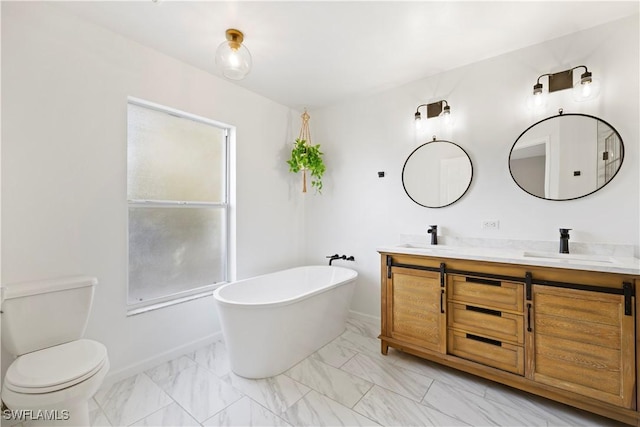 bathroom featuring marble finish floor, double vanity, toilet, a sink, and a freestanding tub