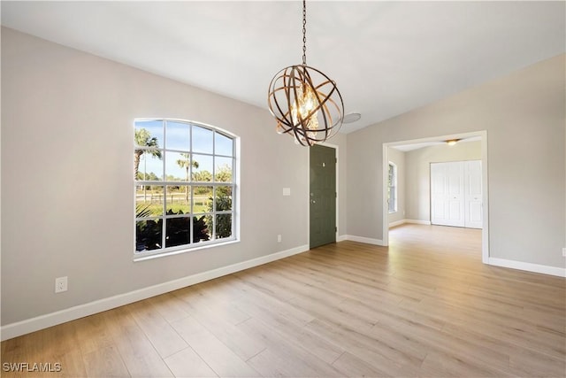 empty room featuring light wood finished floors, baseboards, a chandelier, and vaulted ceiling