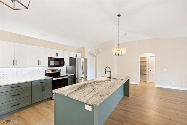 kitchen featuring arched walkways, stainless steel appliances, light stone counters, and light wood-type flooring