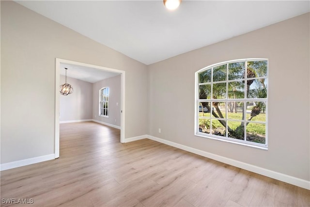 unfurnished room with lofted ceiling, baseboards, wood finished floors, and a notable chandelier