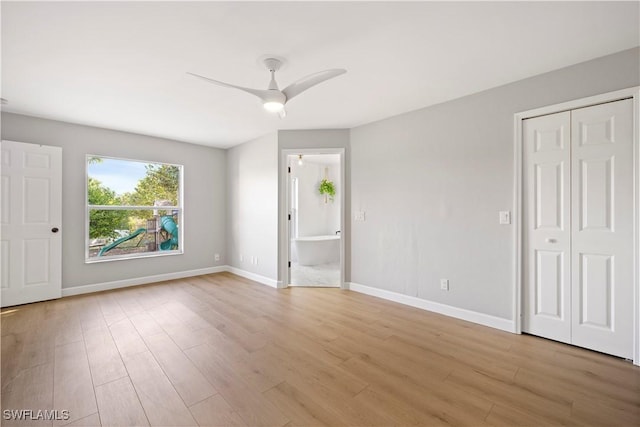 unfurnished bedroom with baseboards, a ceiling fan, ensuite bath, light wood-style flooring, and a closet