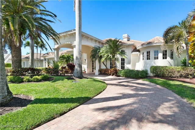 view of front of home featuring stucco siding, a tile roof, decorative driveway, a front yard, and a chimney