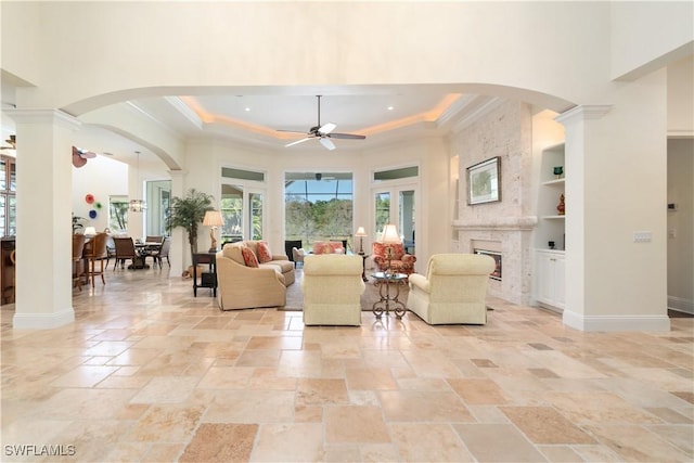 living room featuring built in shelves, a fireplace, a tray ceiling, and decorative columns