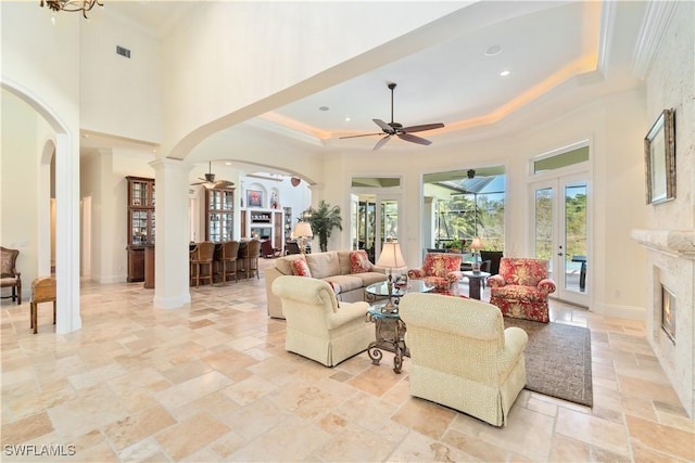 living room with baseboards, ceiling fan, arched walkways, a glass covered fireplace, and a raised ceiling