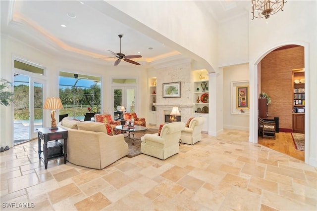 living area featuring stone tile floors, built in features, baseboards, a tray ceiling, and a fireplace