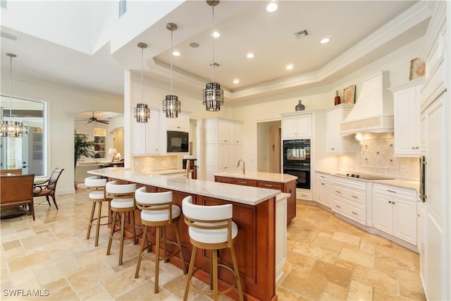 kitchen featuring visible vents, premium range hood, stone tile floors, black appliances, and a raised ceiling