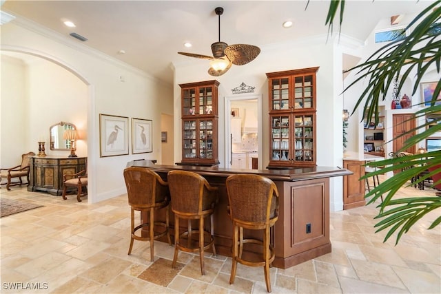 bar featuring visible vents, crown molding, a dry bar, arched walkways, and stone tile flooring