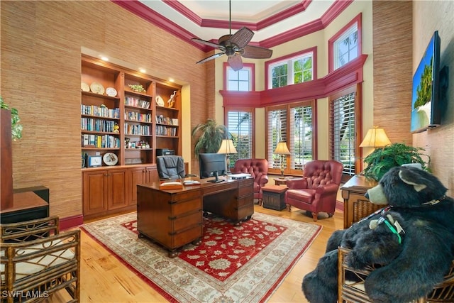 office with built in shelves, a ceiling fan, light wood finished floors, a high ceiling, and crown molding