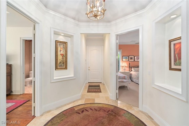 corridor with light tile patterned floors, baseboards, crown molding, and an inviting chandelier