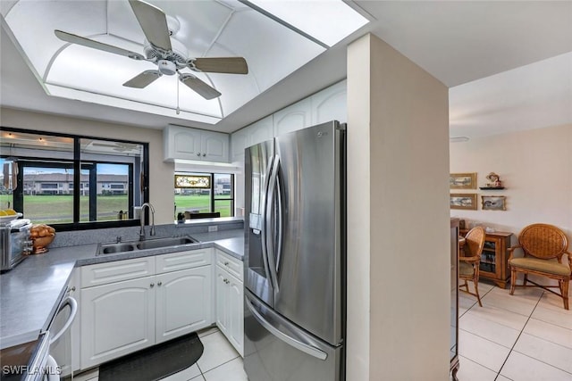 kitchen featuring light tile patterned floors, a ceiling fan, white cabinetry, a sink, and stainless steel fridge