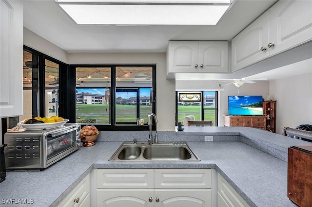 kitchen with a skylight, a toaster, a ceiling fan, white cabinets, and a sink