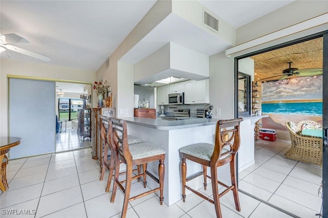 kitchen featuring stainless steel appliances, visible vents, light tile patterned flooring, ceiling fan, and a kitchen bar