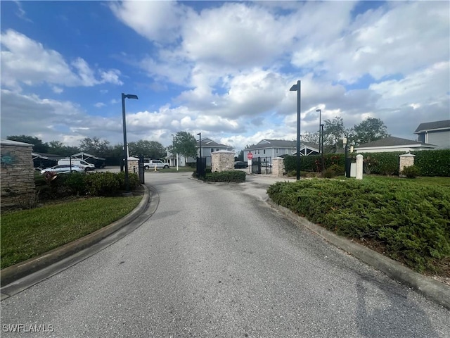 view of road featuring curbs, traffic signs, street lighting, and a gate