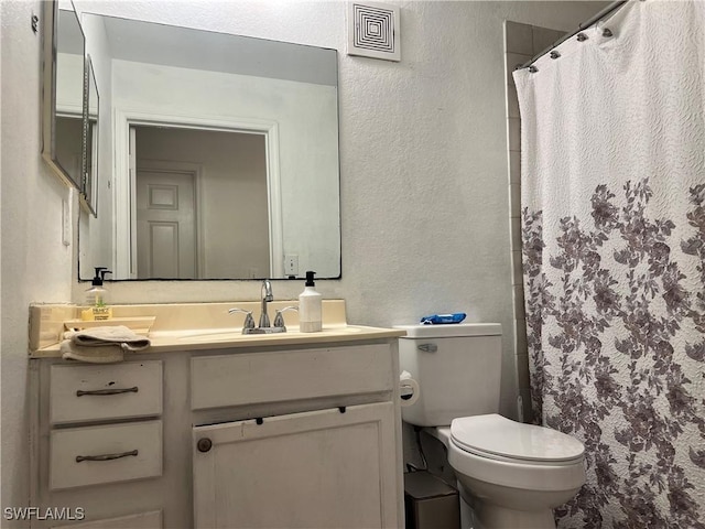 bathroom featuring visible vents, toilet, vanity, and a textured wall