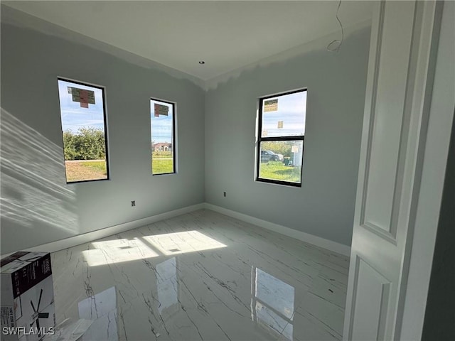 empty room with marble finish floor, plenty of natural light, and baseboards