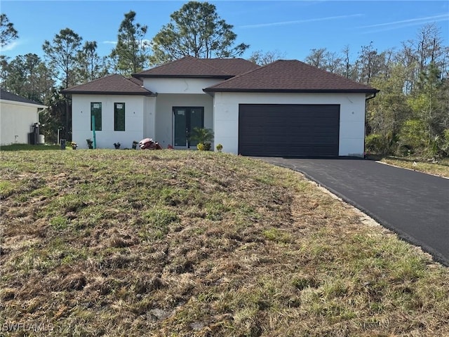 view of front facade with french doors, stucco siding, a shingled roof, a garage, and driveway