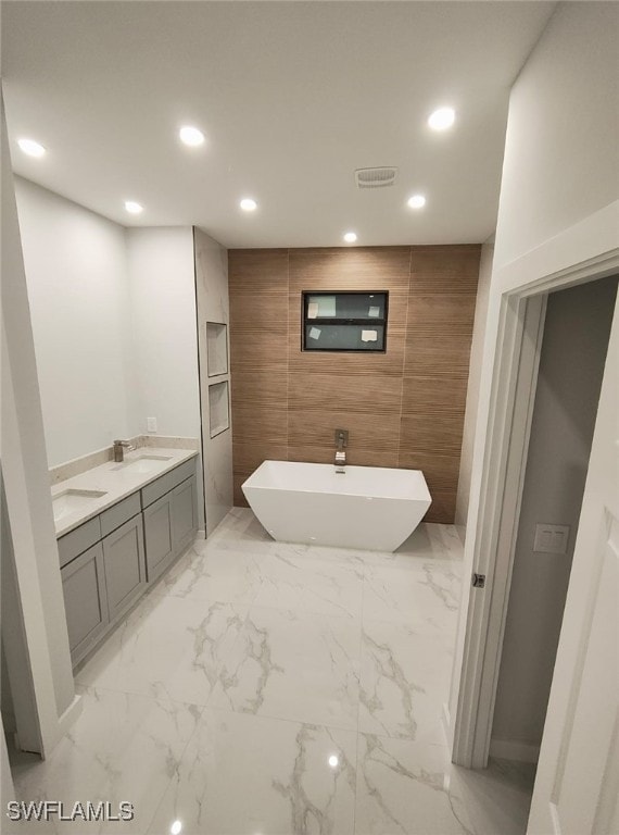 bathroom featuring double vanity, marble finish floor, a freestanding bath, a sink, and recessed lighting