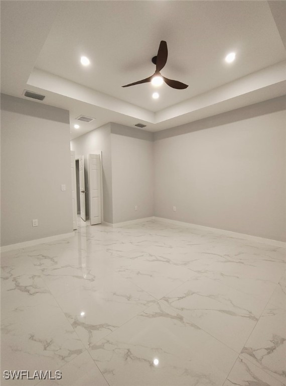 spare room featuring a tray ceiling, visible vents, and baseboards