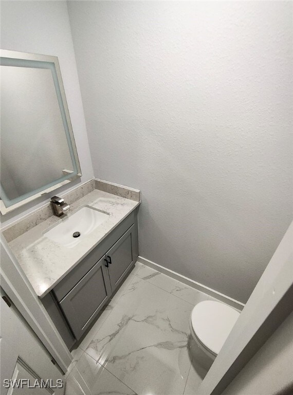 bathroom featuring toilet, marble finish floor, vanity, and baseboards