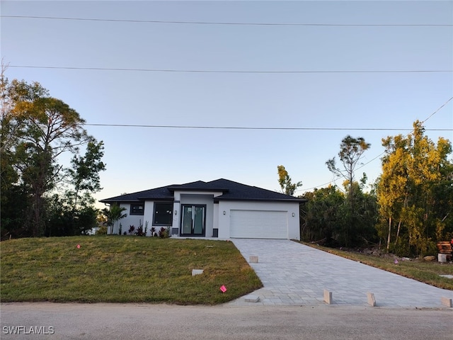 view of front of property with a garage, decorative driveway, a front lawn, and stucco siding