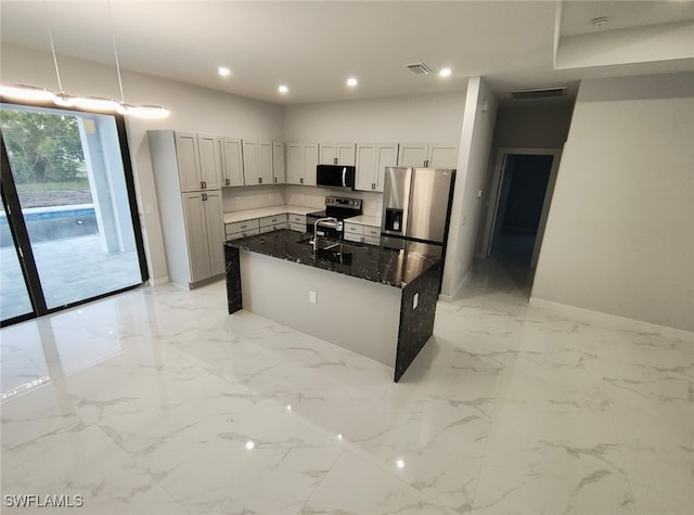 kitchen featuring marble finish floor, a center island with sink, visible vents, appliances with stainless steel finishes, and dark stone counters