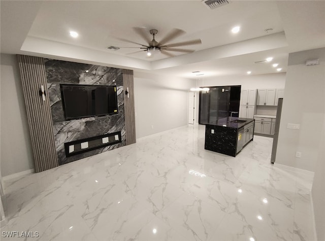 living area with marble finish floor, visible vents, a raised ceiling, and a ceiling fan