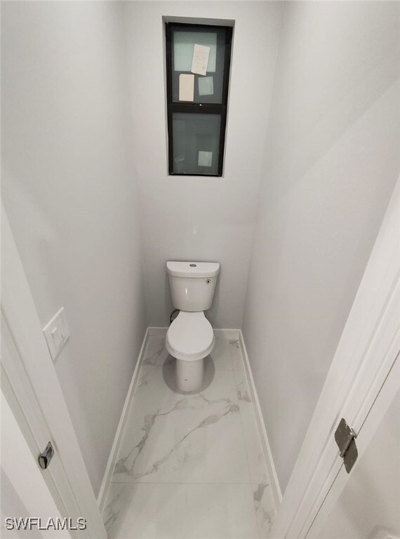 bathroom featuring toilet, marble finish floor, and baseboards