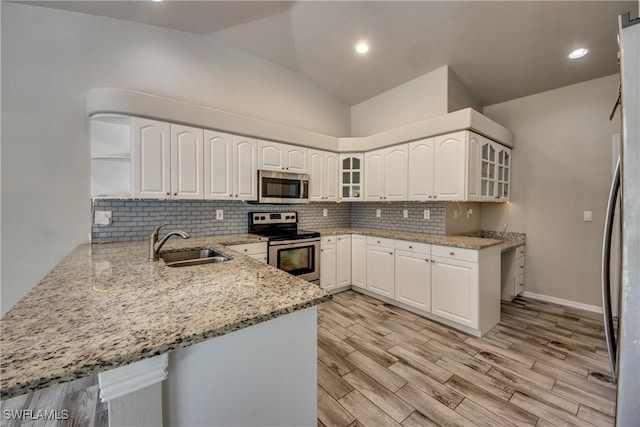 kitchen featuring light stone counters, tasteful backsplash, appliances with stainless steel finishes, a sink, and a peninsula