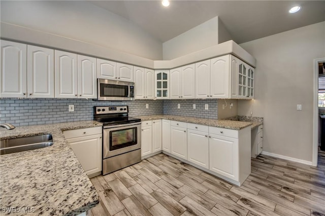 kitchen featuring vaulted ceiling, stainless steel appliances, a sink, and light stone countertops