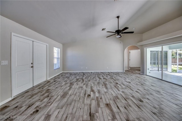 unfurnished living room with arched walkways, vaulted ceiling, wood finished floors, and a wealth of natural light