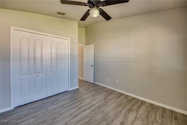 unfurnished bedroom with a closet, visible vents, a ceiling fan, wood finished floors, and baseboards