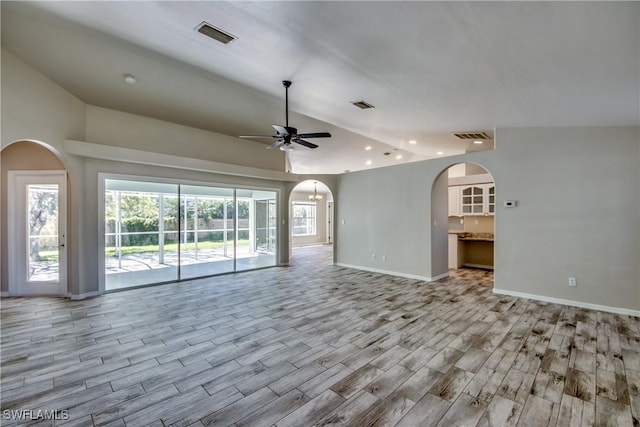 unfurnished living room featuring arched walkways, vaulted ceiling, wood finished floors, and visible vents